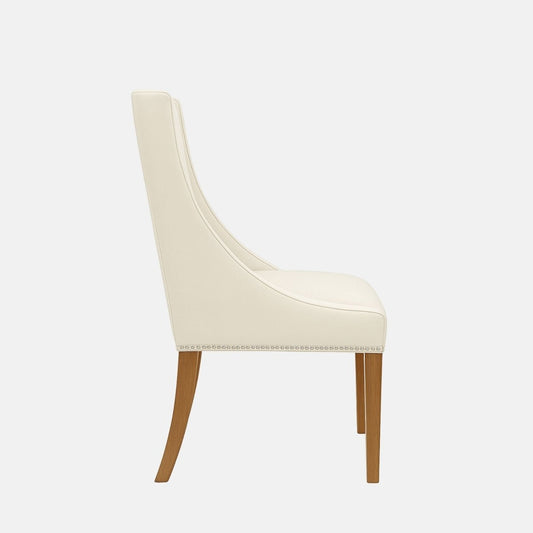 Upholstered dining chair in cream fabric with a gently curved backrest, featuring a geometric patterned fabric panel in beige and gold tones, nailhead trim along the seat base, and natural wooden legs, shown on a white background