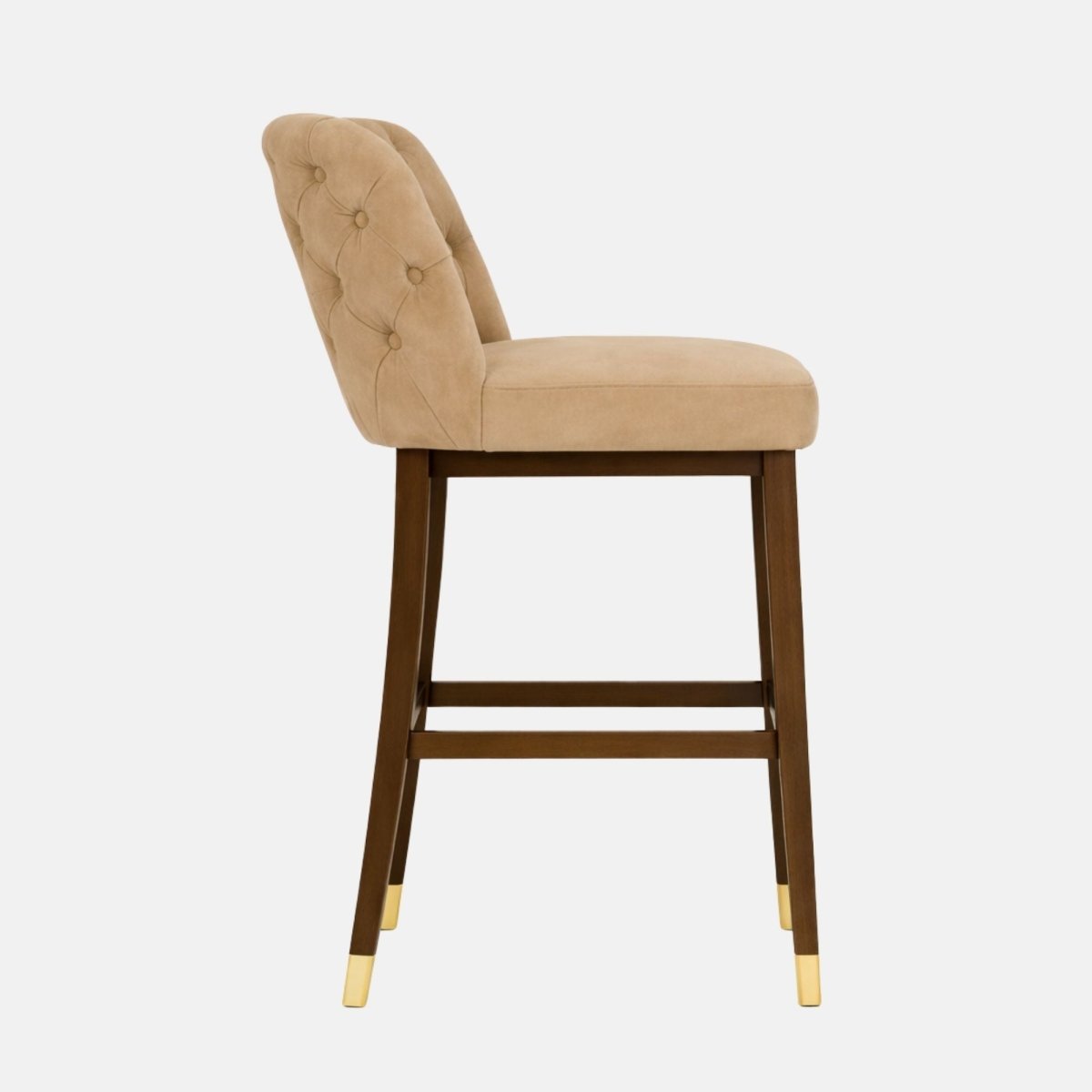 Side profile of a beige, button-tufted upholstered bar stool with a thick seat cushion, dark wooden legs, and brass leg caps, photographed on a white background.