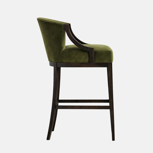 Olive-green upholstered bar-height stool shown in side profile, with a gently sloped back and slim integrated wooden arms, set on a dark wood frame with four legs and a stretcher, photographed on a white background.