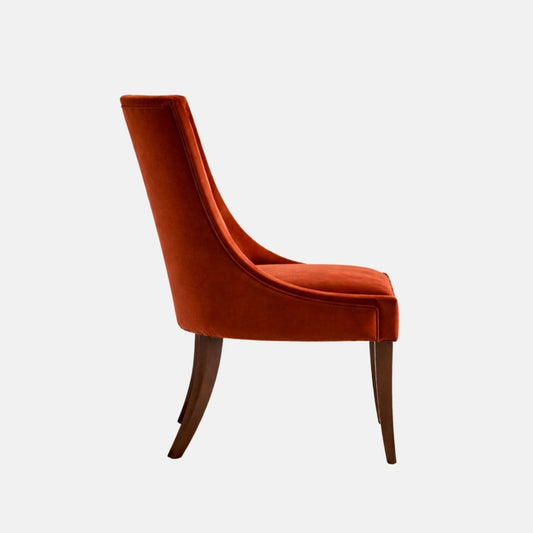 Upholstered accent chair in rust-orange velvet with a patterned fabric panel on the inner backrest, curved arms, cushioned seat, and dark wooden legs, shown against a white background