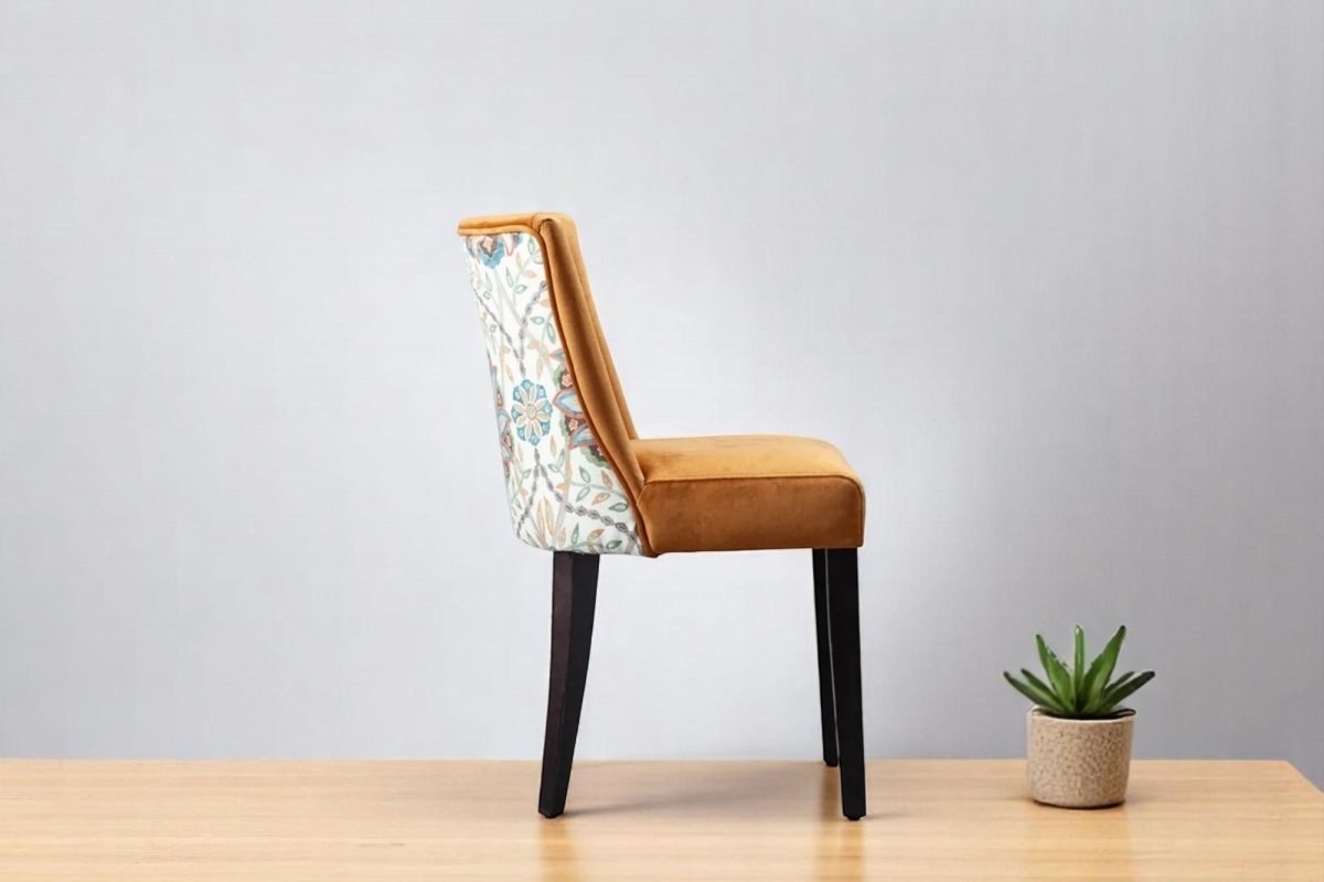 alt="Mustard velvet dining chair with curved backrest, contrasting floral fabric, and black legs"