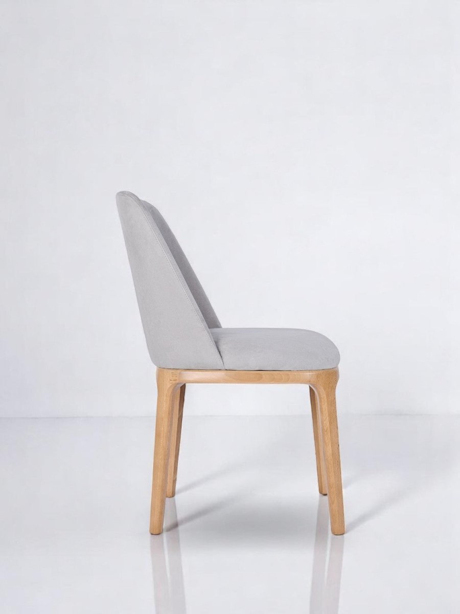 alt="Elegant grey upholstered dining chair with curved back and warm natural oak base"
