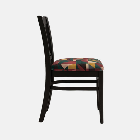 A black wooden dining chair with an X-shaped backrest and straight tapered legs. The seat is upholstered in a bold geometric fabric with red, green, gold, and beige shapes, creating a striking contrast against the matte black frame. Photographed on a light background with realistic shadows.