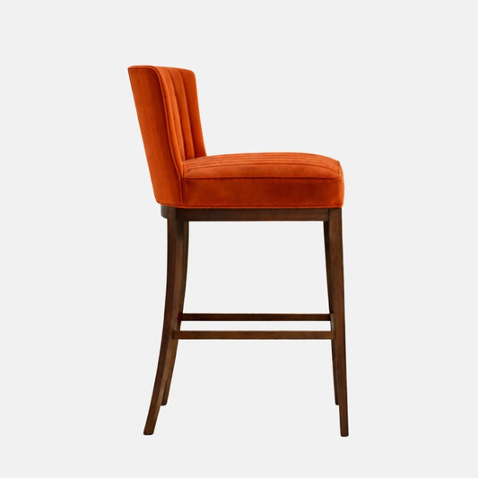 Bar-height stool upholstered in burnt orange velvet with a tall, slightly curved channel-stitched back and a thick cushioned seat, supported by a dark wood four-leg frame with square stretchers/footrest rails, photographed on a white background.