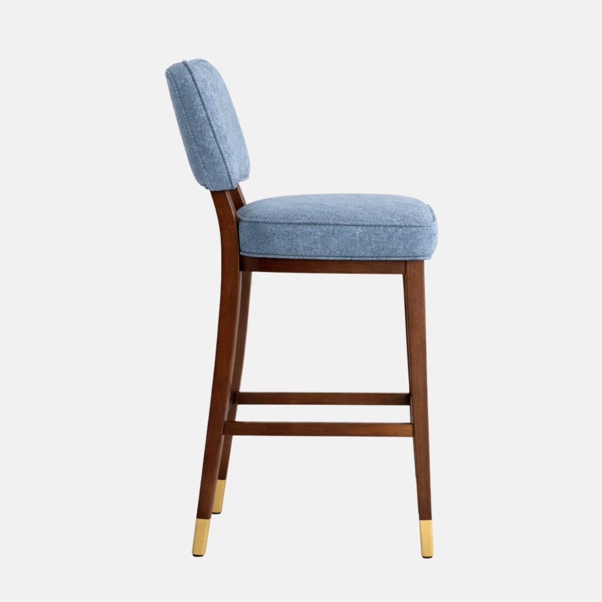 Side view of a blue patterned upholstered bar stool with a padded back and seat, dark wooden legs with lower stretcher rails, and brass leg caps.