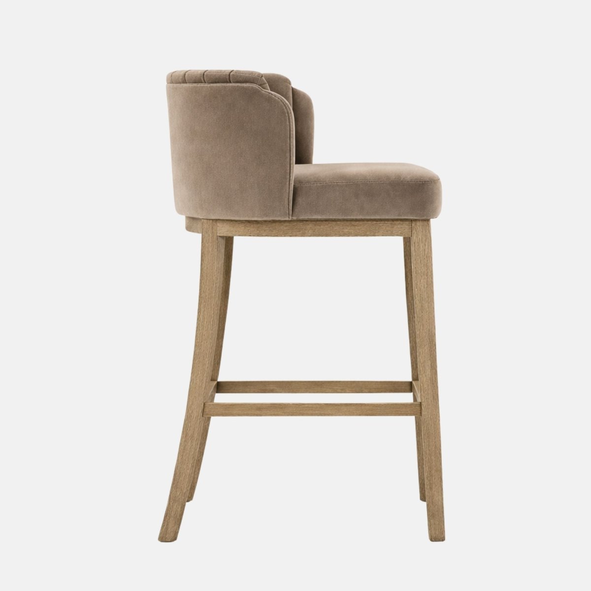 Side profile of a taupe upholstered bar stool with a low wraparound back and thick padded seat, set on light oak wooden legs with a rectangular footrest rung, photographed on a white background.