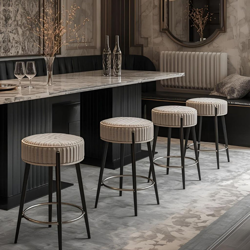 The image shows four stools in a row against a beige background: a zebra-patterned round stool with slim black legs, a blue tufted stool with a wooden frame, a beige padded stool with a gold backrest, and a tall beige round stool with a black frame