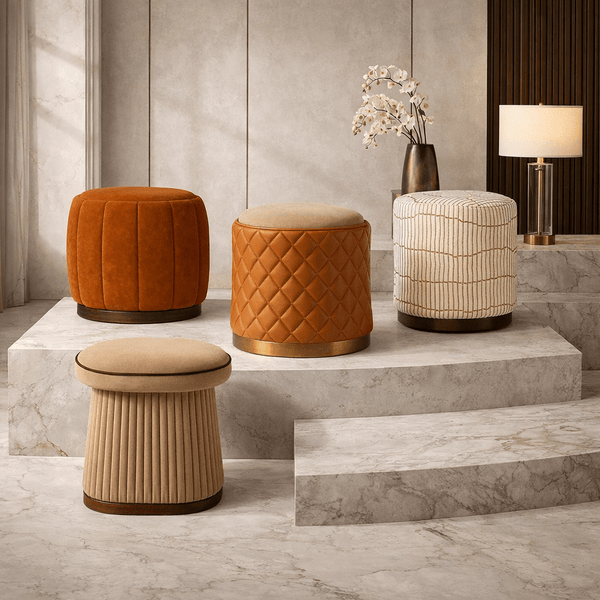 Four ottomans are lined up against a beige backdrop. Designs include: cream hexagon with gold base, geometric brown/taupe with fringe, golden velvet checkerboard with smooth base, and off-white with gold line patterns on a dark wood base.