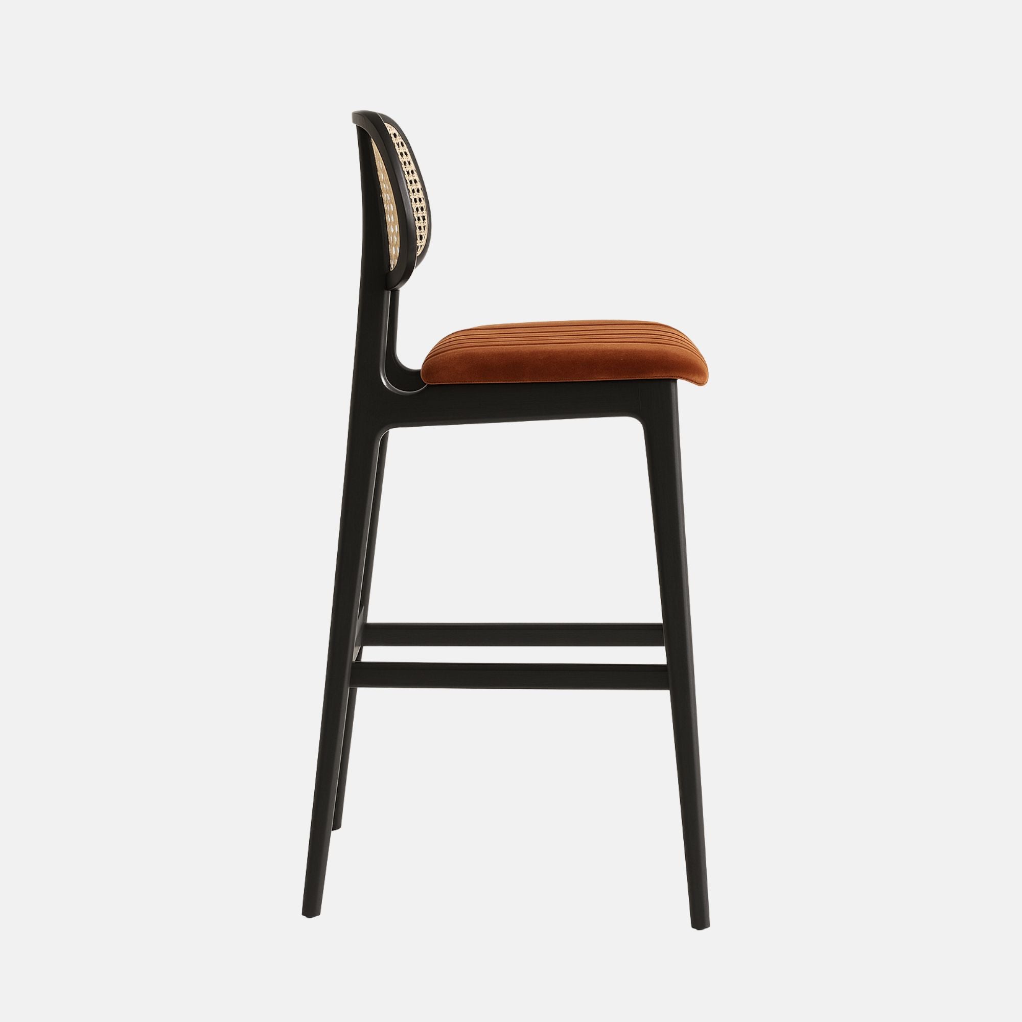 A modern bar stool with a sleek black wooden frame, a woven cane backrest, and a copper velvet upholstered seat featuring fluted detailing, photographed against a plain white background