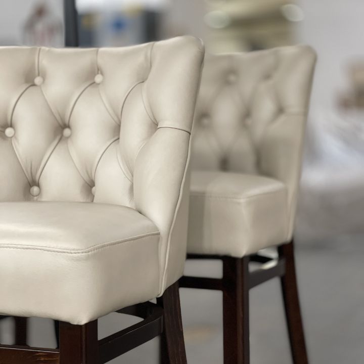 Elegant bar stool with button tufted cream upholstery and wooden legs, featuring a classic Chesterfield design ideal for bars and hospitality interiors