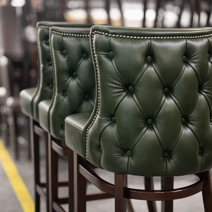 Luxury bar stool with green button tufted leather upholstery and studded trim, featuring wooden legs, ideal for bars and premium hospitality interiors