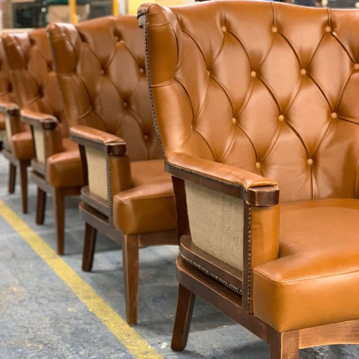 Luxury dining armchair with button tufted leather upholstery and wooden frame, featuring padded arms, ideal for restaurants and premium interiors