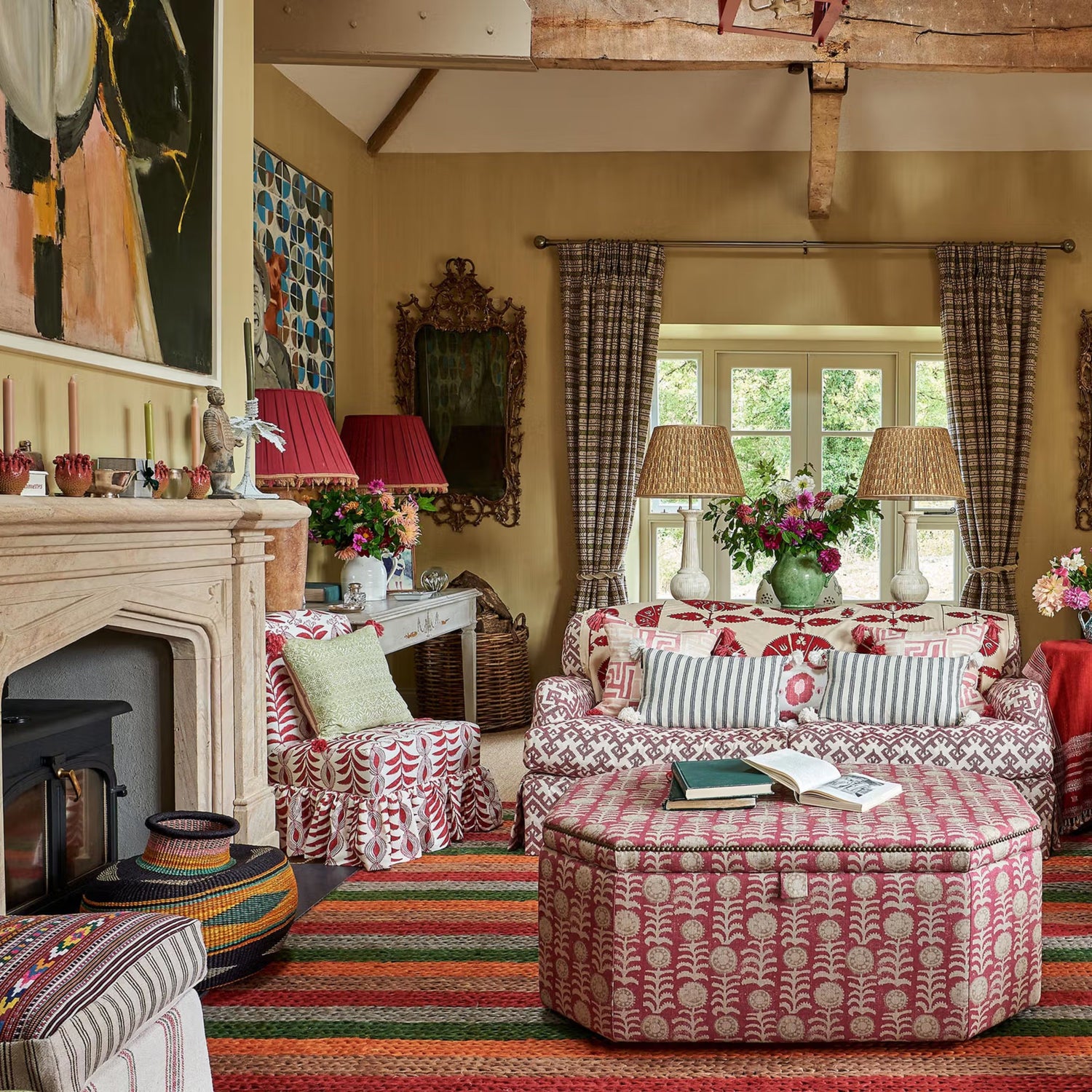 Warm country living room with patterned red and white sofas, matching ottoman, striped rug, stone fireplace, and eclectic vintage decor accents.