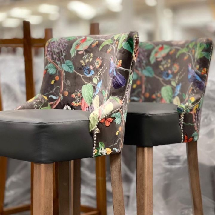 Stylish bar stool with floral patterned fabric backrest and black leather seat, featuring wooden legs, ideal for bars and hospitality interiors