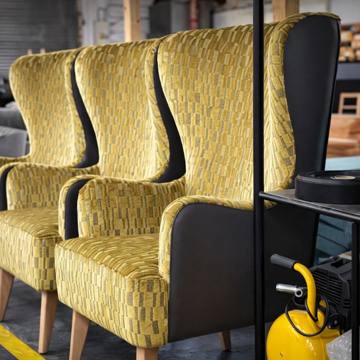 High back lounge chair with yellow patterned upholstery and contrast side panels, featuring wooden legs, ideal for hotels and hospitality interiors