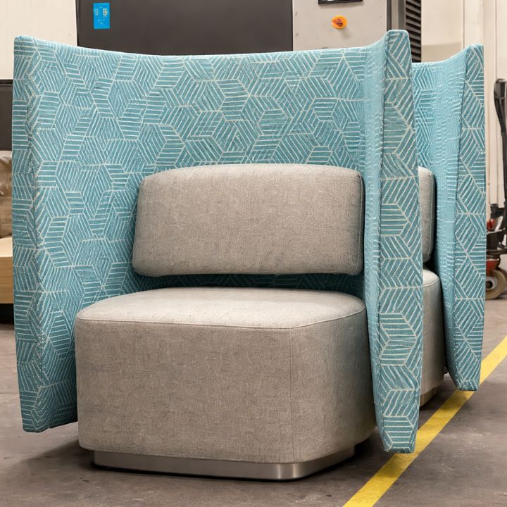 Modern lounge chair with a light upholstered seat and high winged sides in patterned blue fabric, designed for privacy in a showroom setting.