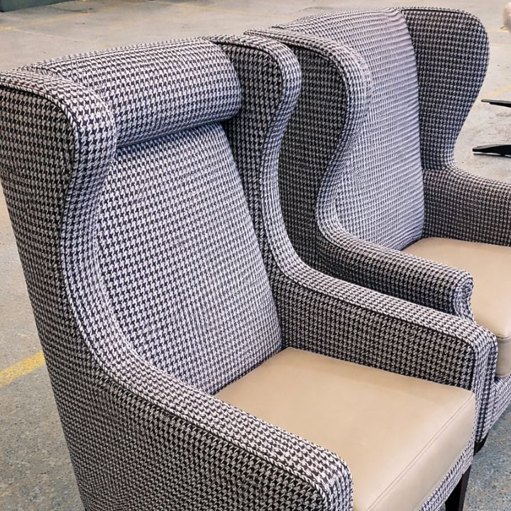 High back wingback lounge chairs upholstered in patterned fabric with curved arms and light upholstered seats in a showroom setting.