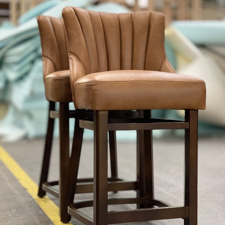 Modern bar stool with brown leather upholstery and ribbed backrest, featuring a wooden frame and footrest, ideal for bars and hospitality interiors