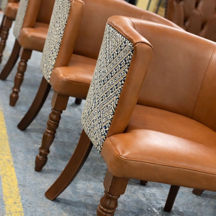 Dining chair with brown leather seat and backrest featuring patterned fabric rear panel, supported by wooden legs, ideal for restaurant and hospitality interiors
