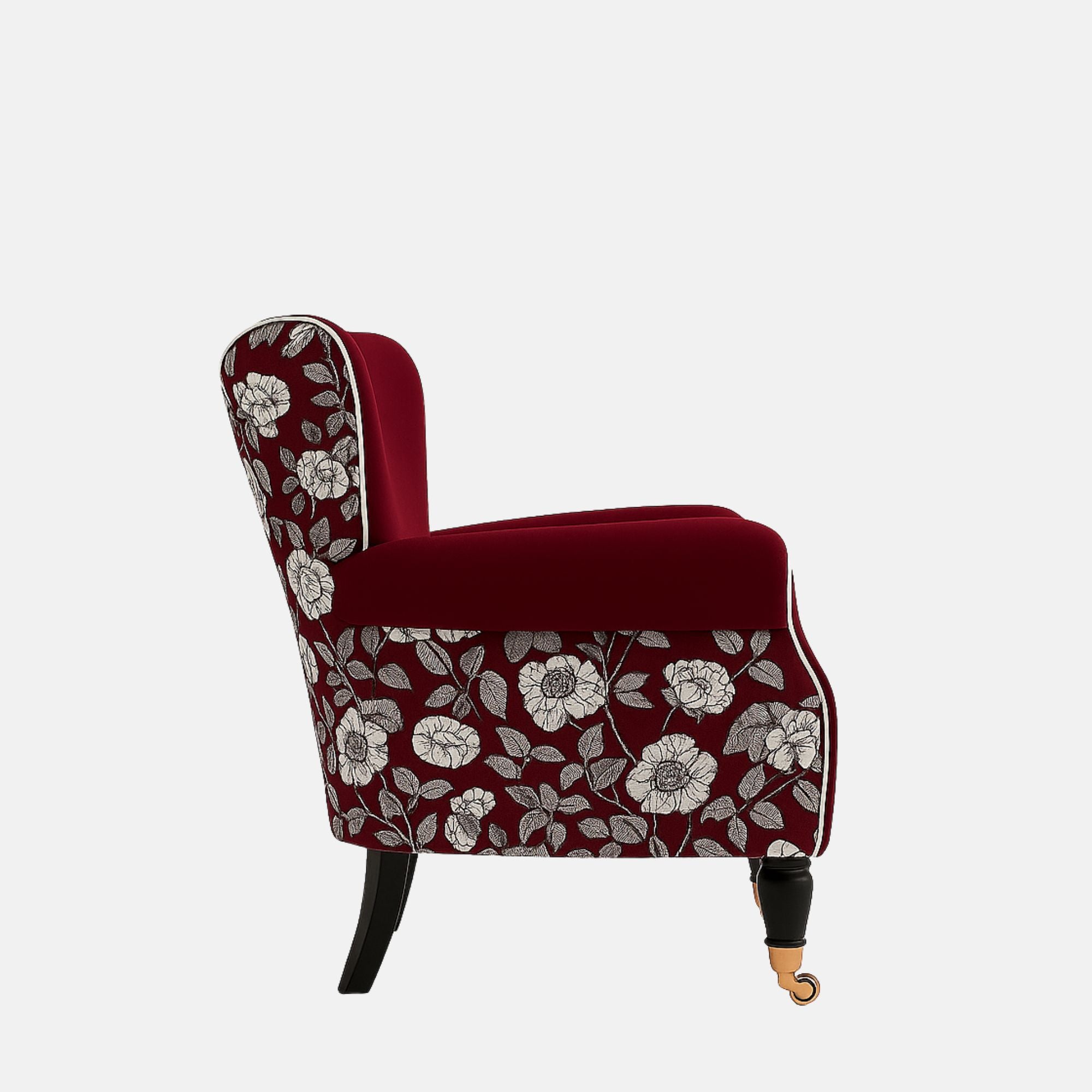 Deep red upholstered armchair with white piping, rolled arms, floral patterned fabric on the back and sides, black legs, and brass front castors.