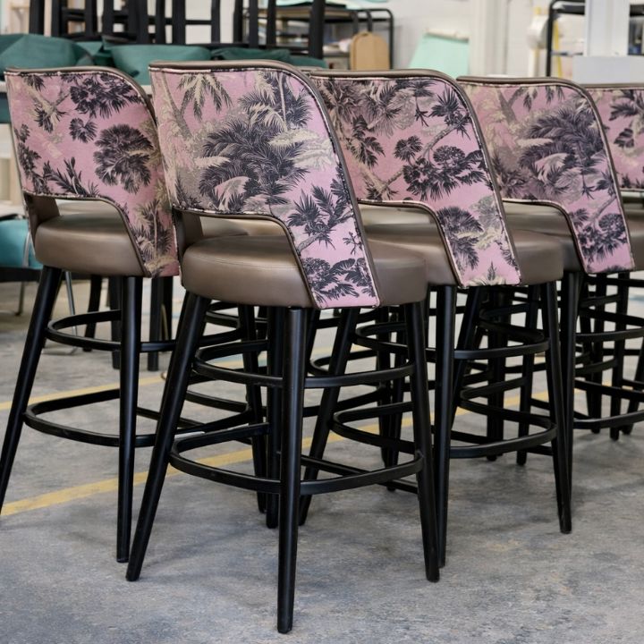 Modern bar stools with tropical patterned fabric backs and upholstered seats, featuring black metal legs, ideal for bars and hospitality interiors
