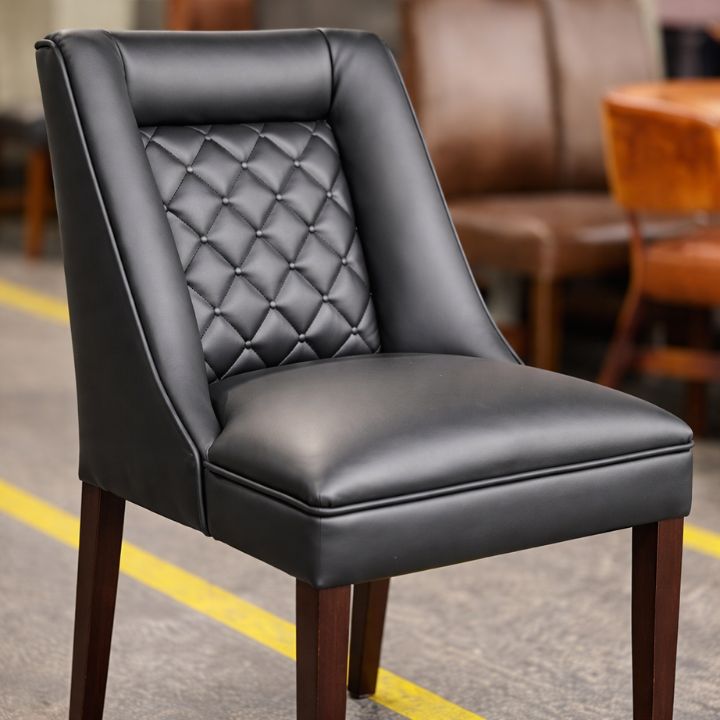 Modern dining chair with black leather upholstery and quilted buttoned backrest, featuring wooden legs, ideal for restaurants and hospitality interiors