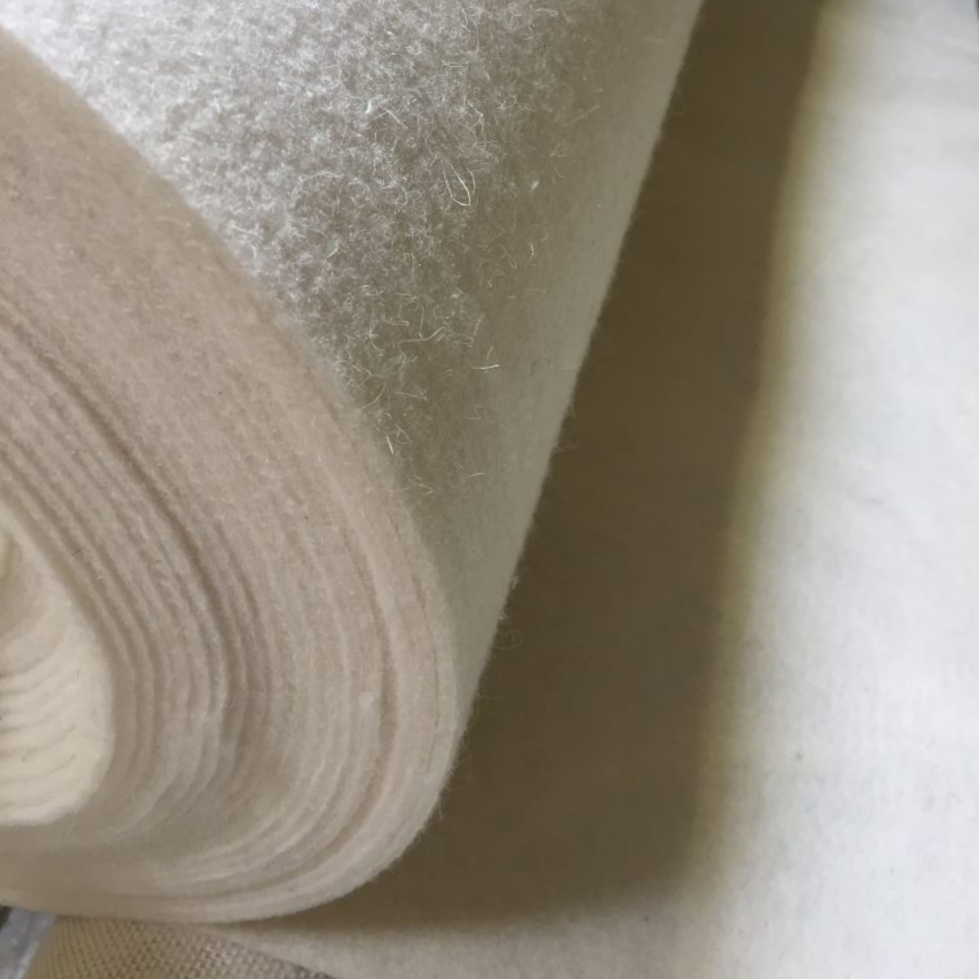 Close-up of a roll of natural wool felt upholstery padding, used as eco-friendly cushioning in handcrafted chairs and bespoke furniture.