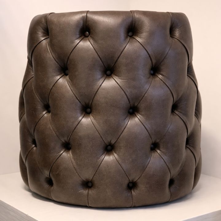 Round brown leather pouffe with deep button tufting placed on a light surface.