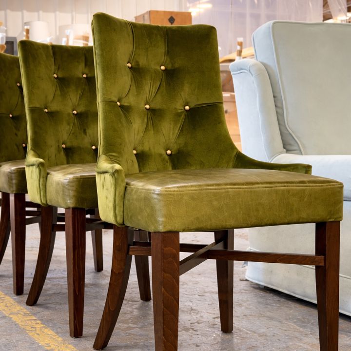Green button-tufted velvet dining chairs with arms and wooden legs displayed in a furniture showroom.
