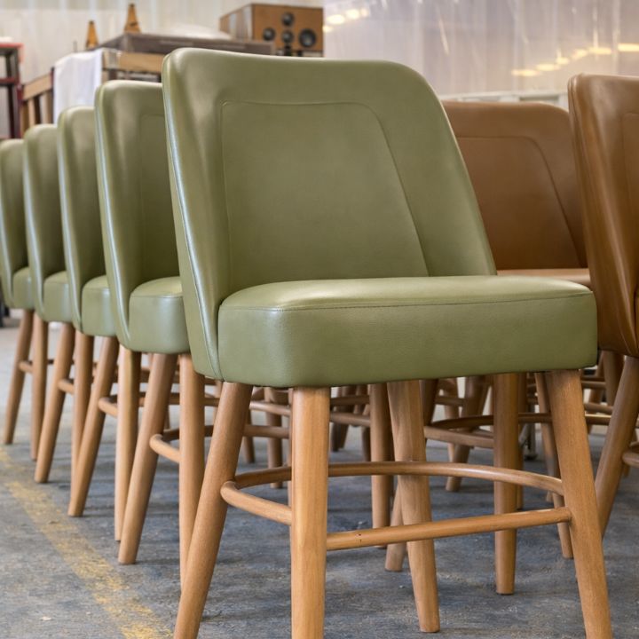 Modern bar stool with olive green upholstered seat and backrest, featuring wooden legs and footrest, ideal for bars and hospitality interiors
