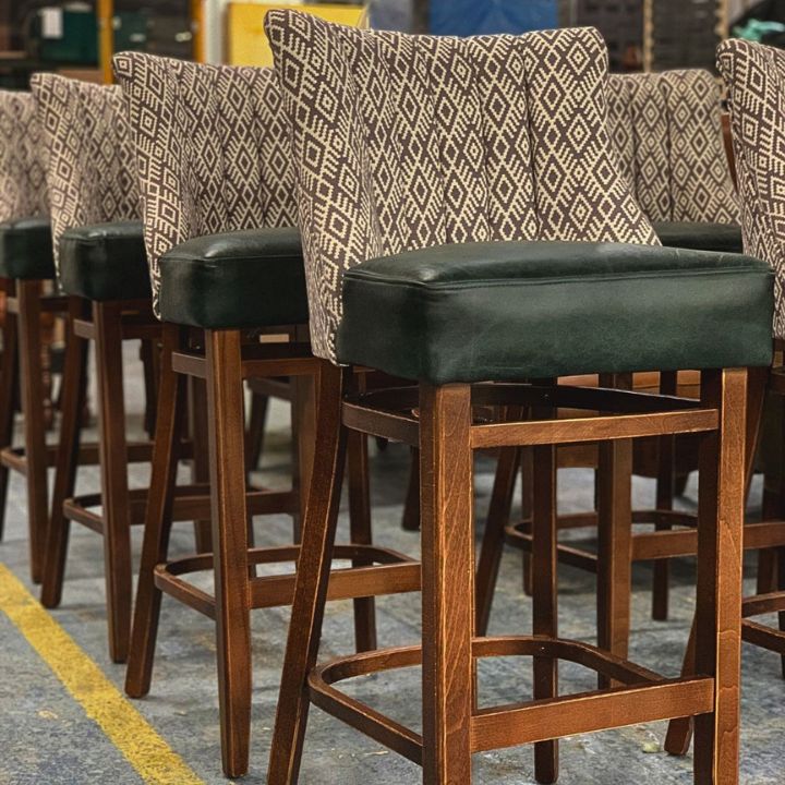 Modern bar stools with patterned fabric backrests and dark upholstered seats, featuring wooden frames and footrests, ideal for bars and restaurant interiors