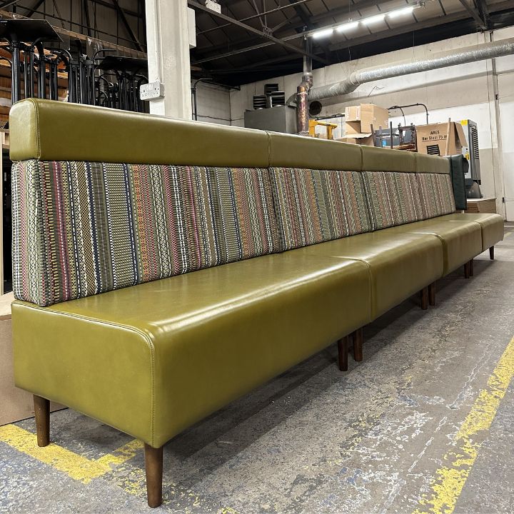 Long upholstered booth seating in olive green with patterned fabric backrest and wooden legs, ideal for restaurant and hospitality interiors