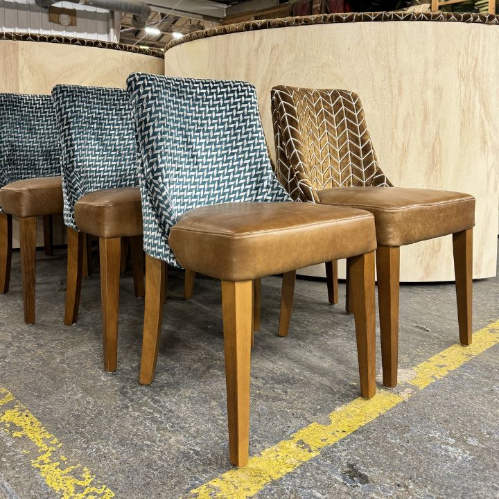 Modern dining chairs with patterned fabric backrests and tan leather seats, featuring wooden legs, suitable for restaurants and hospitality interiors