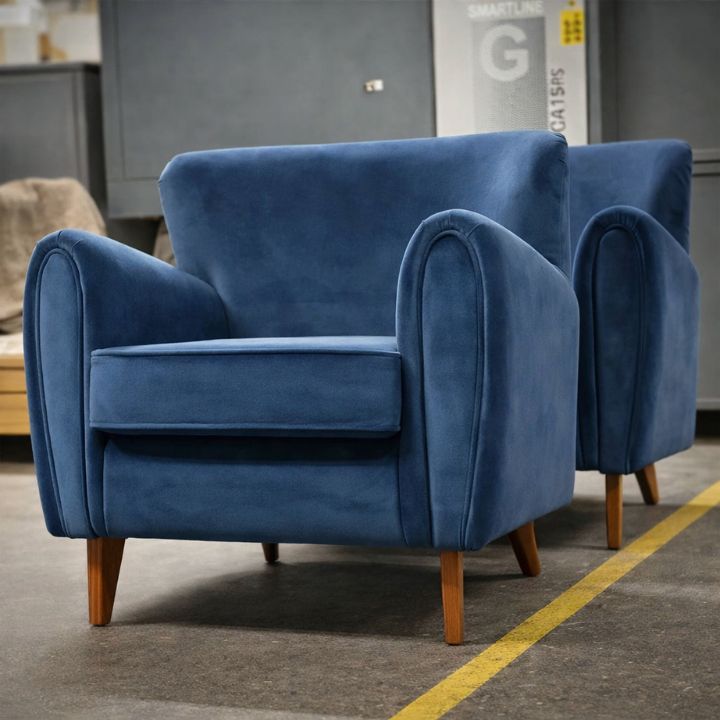 Modern lounge armchair in blue velvet with rounded arms and wooden legs, ideal for hotels, lounges, and stylish interiors