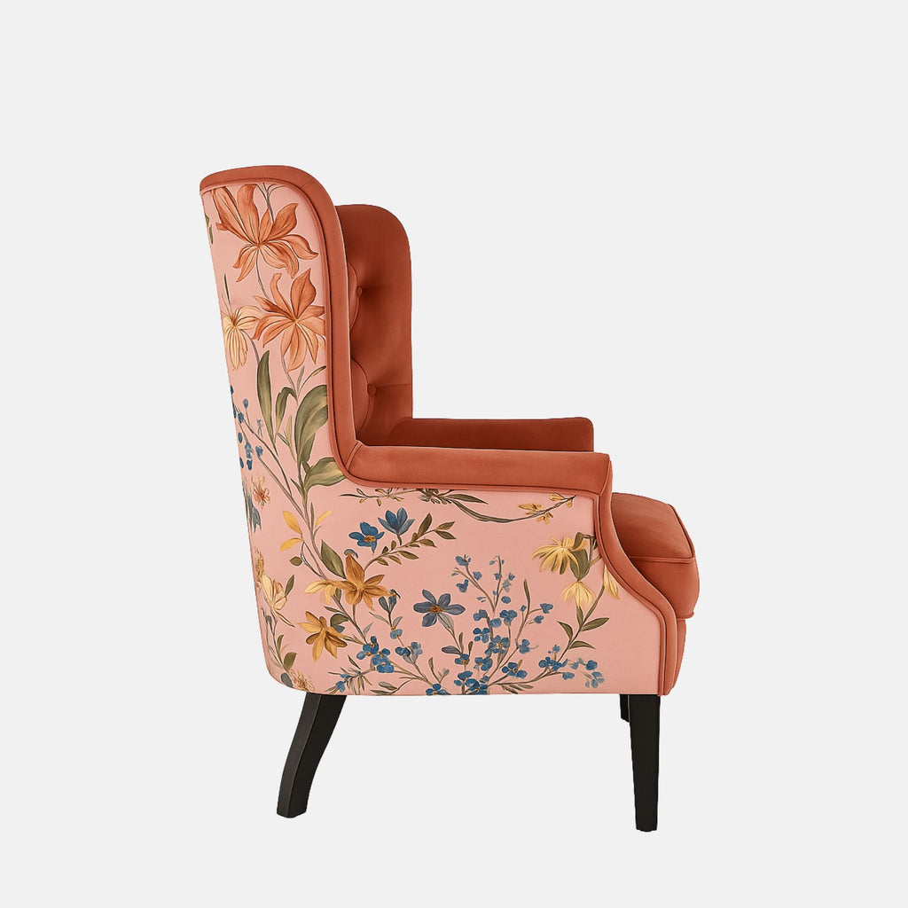 Coral-pink tufted wingback armchair with rolled arms, black legs, and floral patterned fabric on the outer back and sides.