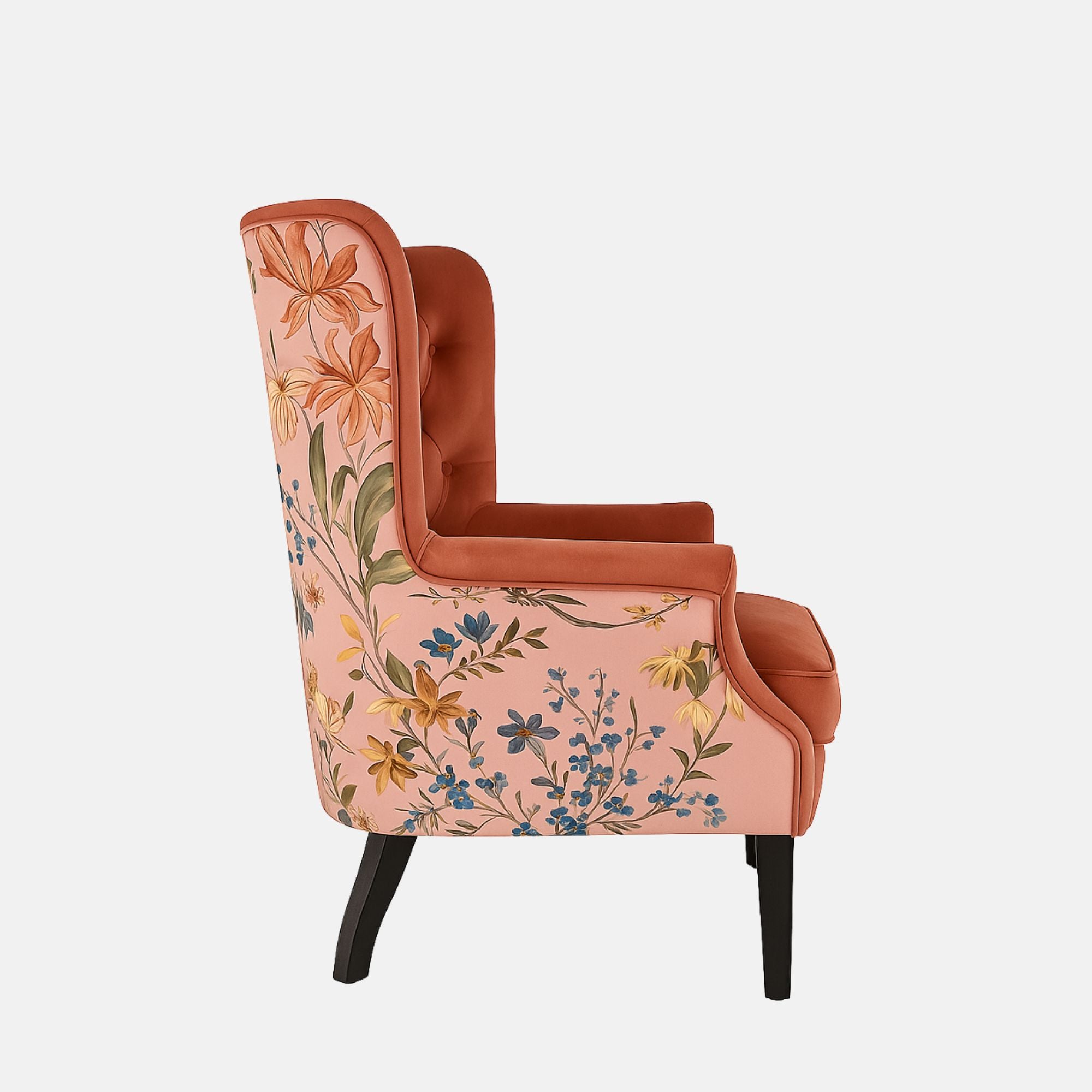 Coral-pink tufted wingback armchair with rolled arms, black legs, and floral patterned fabric on the outer back and sides.