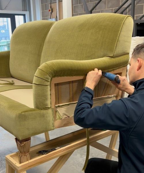 Furniture craftsman attaching green upholstery fabric to an armchair frame