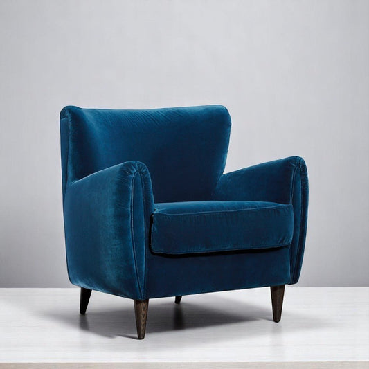 alt="Vintage-style blue velvet lounge chair with a cushiony seat and contrasting black legs"