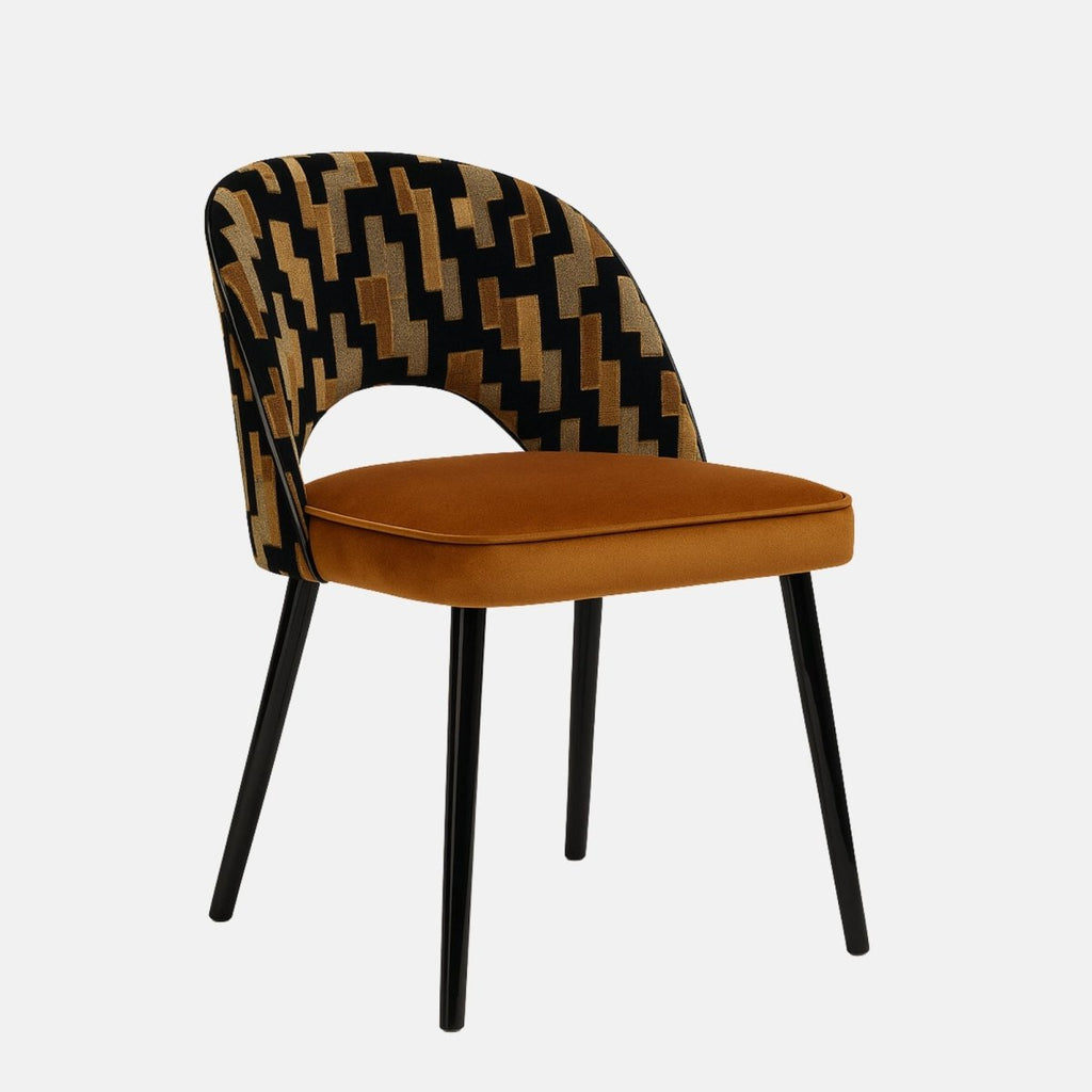 Modern upholstered dining chair with a patterned black, gold, and beige fabric backrest featuring a cut-out design, paired with a rust-orange velvet seat and slim black metal legs, set against a light grey background.