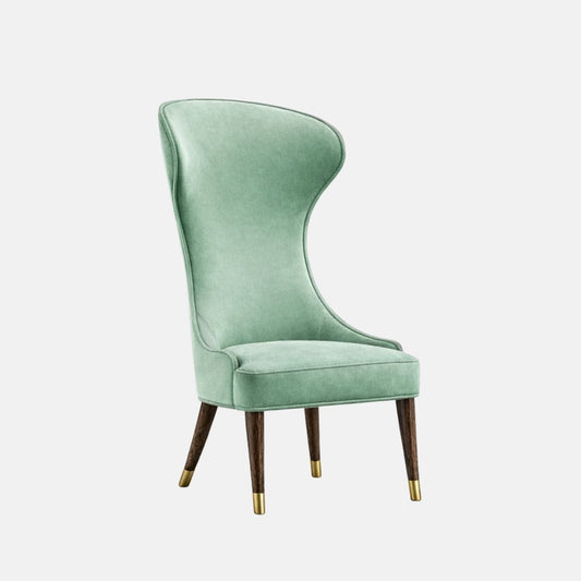 Upholstered accent chair in soft sage-green velvet with a tall, sculpted curved backrest, cushioned seat, and dark wooden legs finished with brass-capped feet, shown on a white background