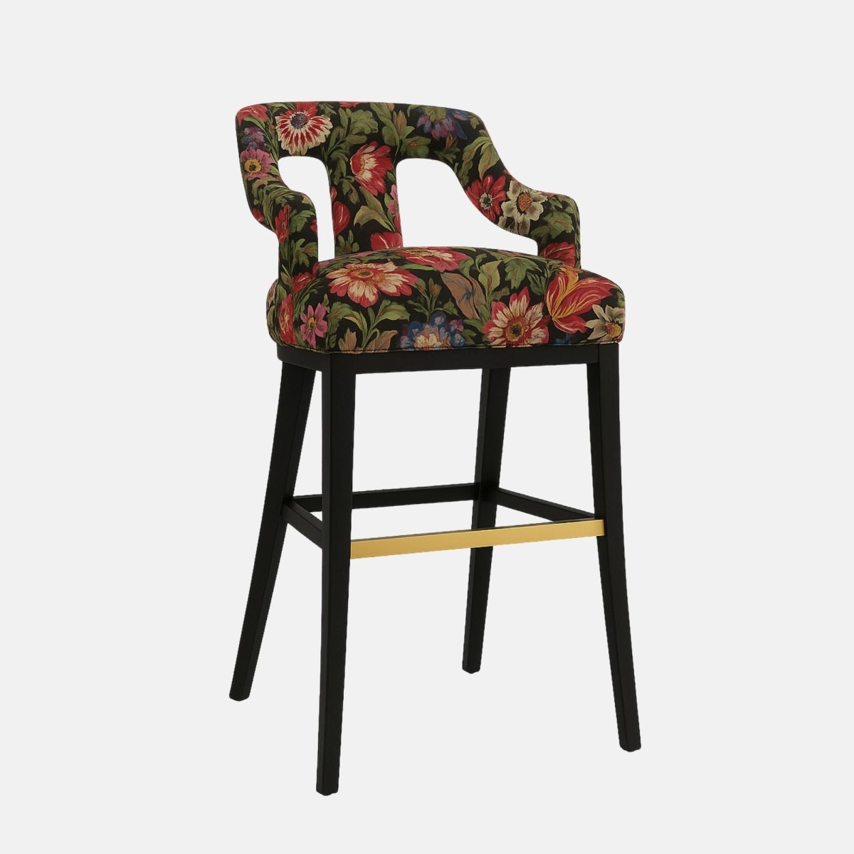 Stylish bar stool with a partially open backrest and curved arm supports, upholstered in a bold floral fabric featuring red, green, and gold tones on a black background. It has a black wooden frame with a brass footrest accent, combining vintage and modern aesthetics