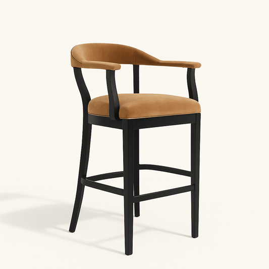 A modern bar stool with a matte black wooden frame and caramel beige velvet upholstery. The chair features curved back legs, a low curved backrest, and padded armrests, all upholstered in matching velvet. The side profile highlights the sleek, ergonomic design and horizontal footrest. The stool is set against a plain off-white background.