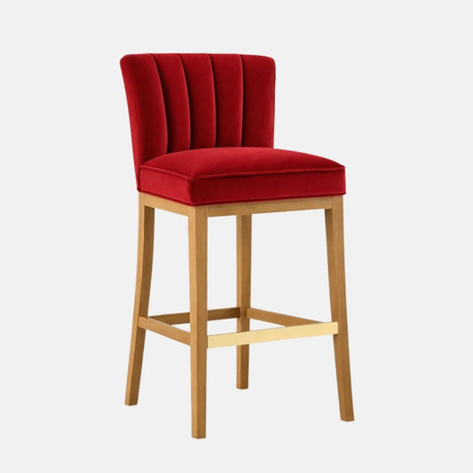 Red velvet bar stool with a channel-tufted backrest, padded seat, and light wood legs with a brass footrest bar.