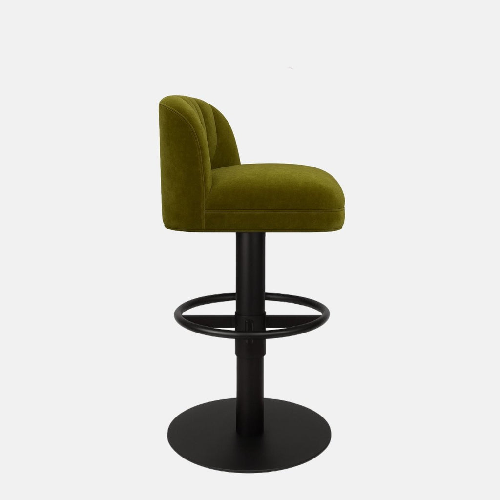 Olive green upholstered bar stool with a low curved backrest featuring vertical channel stitching, black circular footrest, and round black metal base on a white background