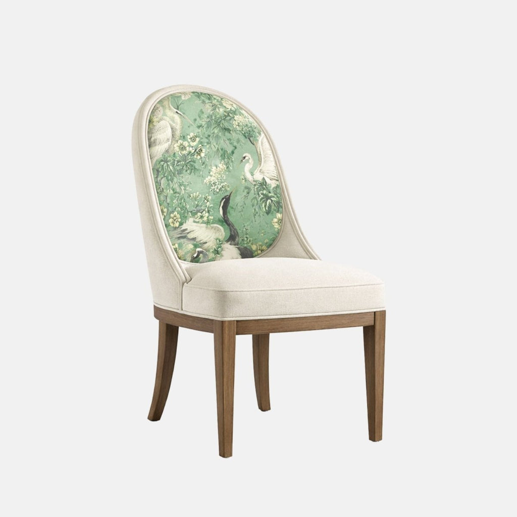 Upholstered accent chair with a cream fabric frame and cushioned seat, featuring a rounded backrest with a green botanical and bird-patterned fabric panel, supported by dark wooden legs, shown on a white background