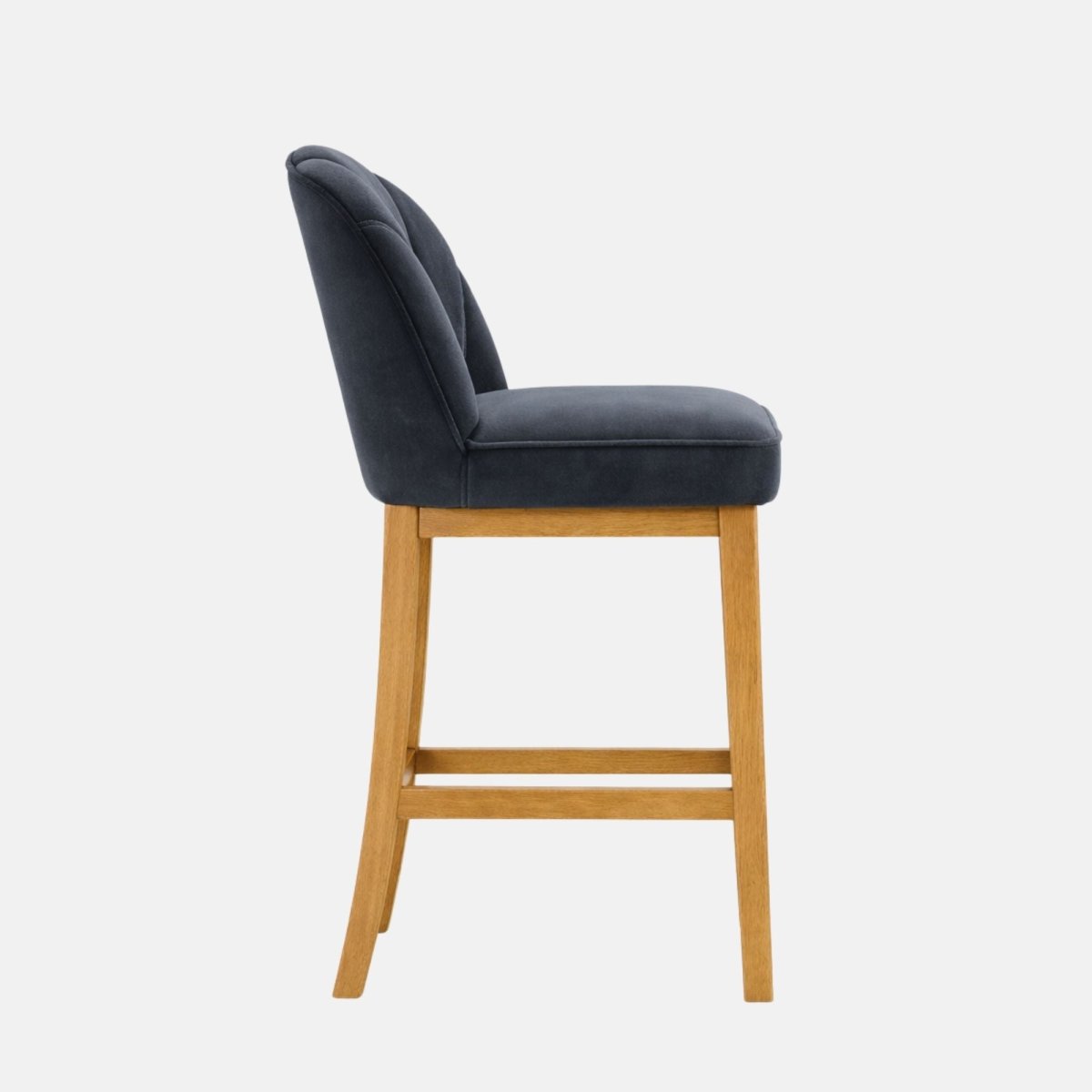 Side view of a dark navy upholstered bar stool with a gently curved back and padded seat, set on light oak wooden legs with a horizontal footrest rail, photographed on a white background.