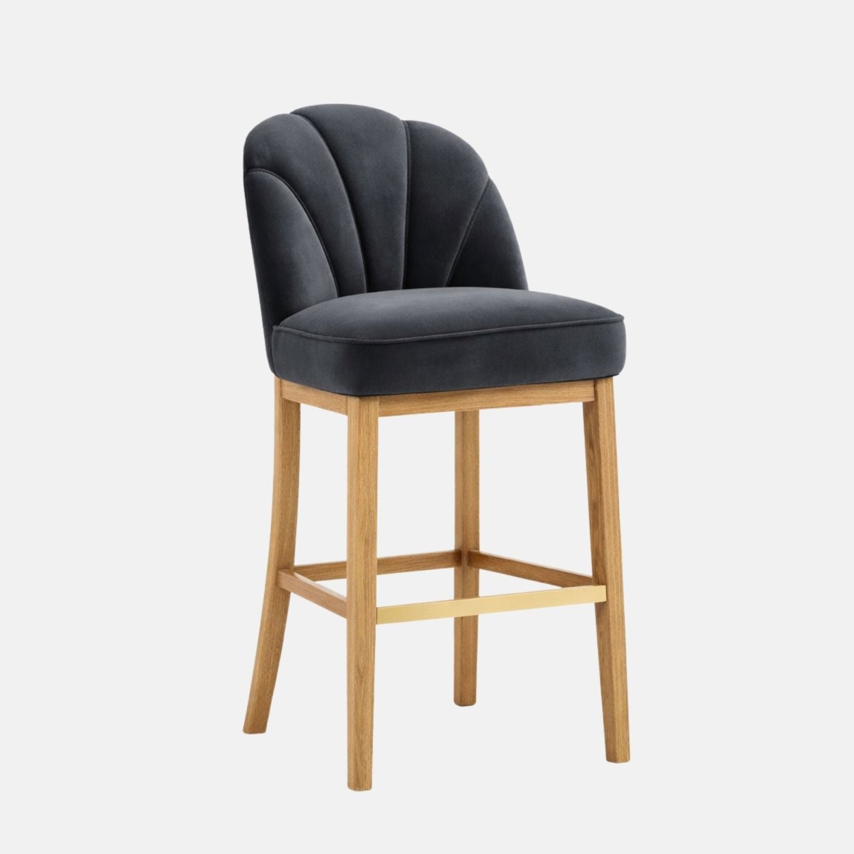 Three-quarter view of a dark charcoal upholstered bar stool with a scalloped, paneled backrest and thick padded seat, on light oak wooden legs with a gold-toned footrest, photographed on a white background.