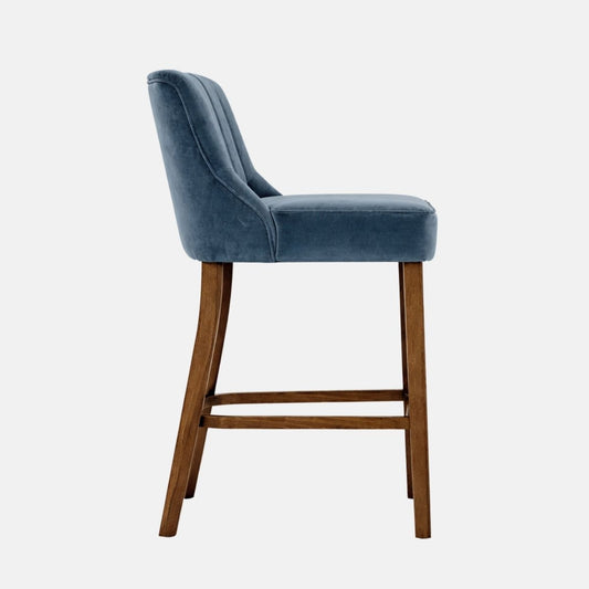 Blue velvet bar stool with channel back design and wooden legs, side view.