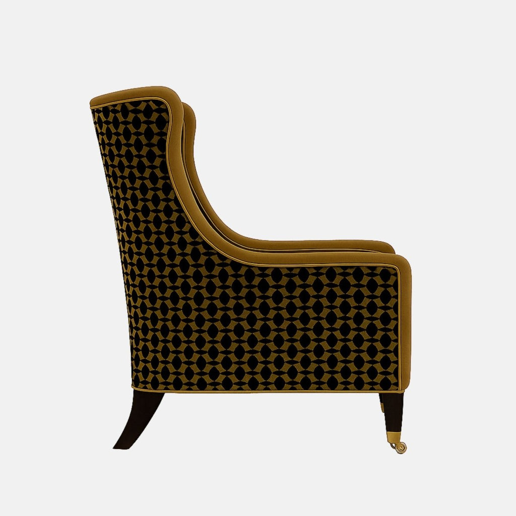 Camel-brown upholstered armchair with gently curved sides, a cushioned seat, black legs with brass castors, and black-and-gold geometric patterned fabric on the outer back and sides