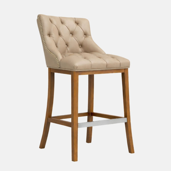 Beige button-tufted upholstered bar stool with nailhead trim, tapered wooden legs, and a metal footrest bar.